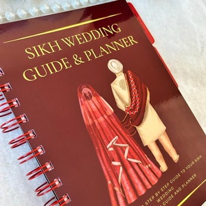 May include: A burgundy spiral-bound Sikh Wedding Guide & Planner. The cover features gold lettering and an illustration of a couple in traditional wedding attire. The book provides a step-by-step guide and information.