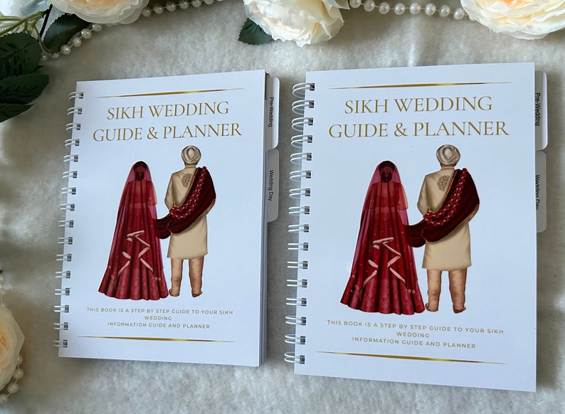 May include: Two spiral bound planners with white covers and gold lettering. The covers feature a cartoon illustration of a Sikh couple in traditional wedding attire. The text on the cover reads "Sikh Wedding Guide & Planner".