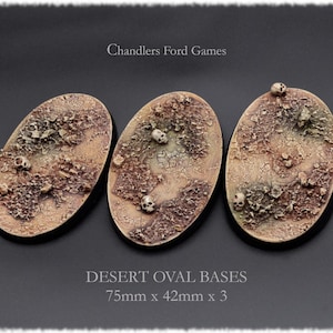 Könnte beinhalten: Drei ovale Wüstenbasen mit strukturierter, rissiger Oberfläche und Miniatur-Schädeln. Die Basen sind 7,5 cm x 4,2 cm groß und für Miniaturspiele konzipiert. Der Text lautet "Desert Oval Bases".