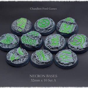Puede incluir: Diez bases redondas de plástico de 32 mm para juegos de miniaturas. Las bases son grises con una superficie texturizada y presentan líneas verdes brillantes en un patrón geométrico. Las bases están etiquetadas "Necron Bases 32mm x 10 Set A".