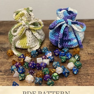 Könnte beinhalten: Zwei gehäkelte Beutel mit Kordelzug, einer grün-weiß, der andere blau-lila, mit einer Vielzahl von bunten Würfeln, die um sie herum verstreut sind. Der Text "PDF PATTERN" befindet sich am unteren Rand des Bildes.