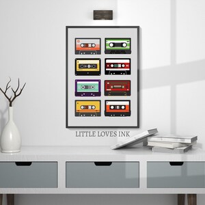 Puede incluir: Una impresi&oacute;n enmarcada con fondo blanco y marco negro que presenta una colecci&oacute;n de nueve cintas de cassette de colores. El texto "LITTLE LOVES INK" est&aacute; impreso debajo de la imagen.