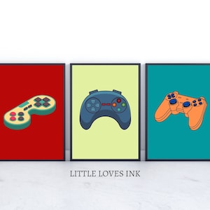 May include: Three framed prints of different coloured backgrounds with a black and white video game controller on each. The controllers are different styles. The first is red, the second is yellow, and the third is blue.