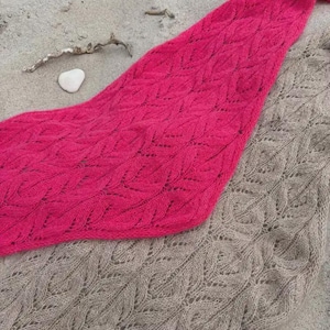 Op de afbeelding: Twee gebreide sjaals met een ingewikkeld bladachtig kantpatroon. De ene sjaal is felroze van kleur, terwijl de andere een neutrale beige tint heeft. Beide items vertonen een delicate, opengewerkte textuur door het gedetailleerde breiwerk.