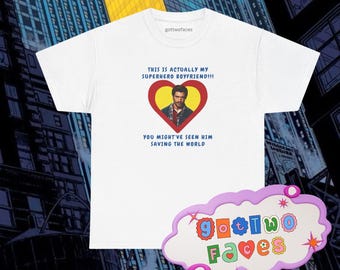 May include: White t-shirt with the text "THIS IS ACTUALLY MY SUPERHERO BOYFRIEND!!!" and "YOU MIGHT'VE SEEN HIM SAVING THE WORLD". The shirt features a heart-shaped graphic with a man's portrait. The brand name "gottwofaces" is printed at the top.
