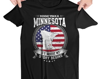 May include: Black t-shirt with a white graphic of the state of Minnesota superimposed on an American flag. The text "Minnetonka Minnesota" and "It's Where My Story Begins" is printed on the shirt.