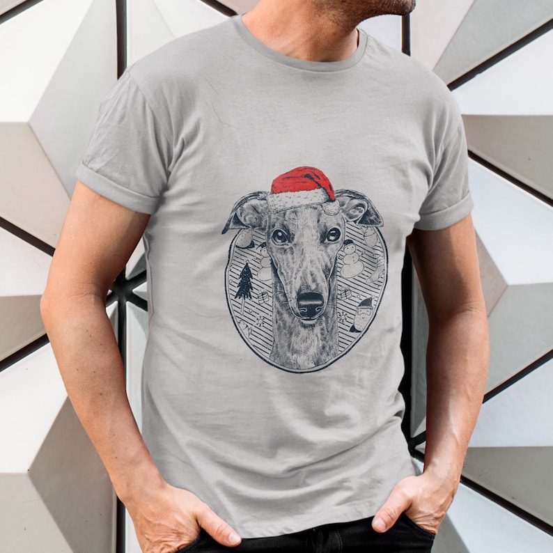 May include: A gray t-shirt with a graphic of a greyhound dog wearing a red Santa hat. The dog is surrounded by a circle with a winter scene, including a Christmas tree, snowmen, and snowflakes.