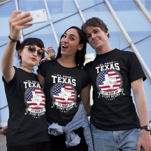 May include: Three people wearing black t-shirts with a graphic of the state of Texas in the shape of a US flag. The text on the shirts reads "El Paso Texas" and "It's where my story begins".