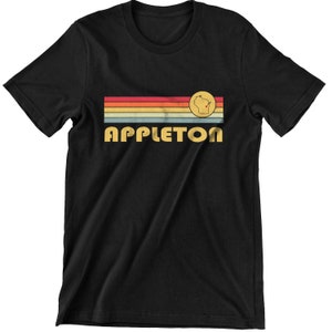 Może przedstawiać: Czarny T-shirt z wzorem w stylu vintage, z paskami w kolorach tęczy i napisem "APPLETON" w żółtych literach. W środku pasków znajduje się koło z zarysowaniem stanu Wisconsin i czerwoną kropką reprezentującą Appleton.
