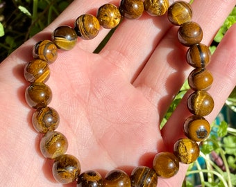 May include: A brown and gold tiger's eye beaded bracelet. The beads are round and have a natural, polished finish.