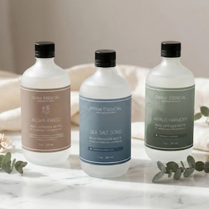 May include: Three clear glass bottles with black caps and labels. The labels read "DIVINA ESENCIAL" and feature text such as "ALOHA KAKOU", "SEA SALT SONG", and "AMALFI HARMONY". Each bottle contains 7 oz / 207 ml of reed diffuser refill.