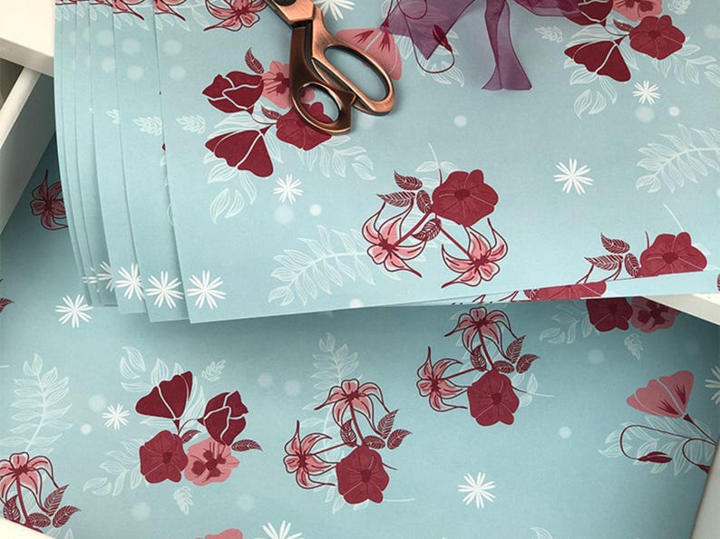 May include: A stack of light blue wrapping paper with a white floral pattern and red flowers. The paper is decorated with white snowflakes.