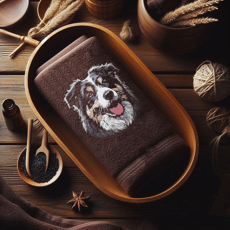 Stickmotiv Hundekopf eines dreifarbigen Aussies im modernen Sketch-Stil mit wachsamen Augen und rosa Zunge, umgesetzt als stilvolle Dekoration für Wellnessbereiche und Bäder auf einem dunkelbraunen Handtuch von LunaChild.com