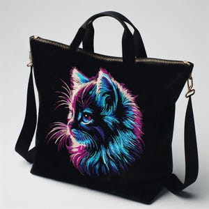 Puede incluir: Bolso tote de lona negra con una imagen bordada de colores de la cara de un gato. El pelaje del gato es una mezcla de azul, morado y rosa.