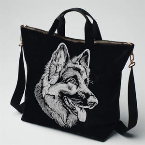 May include: A black tote bag featuring a detailed white embroidered portrait of a German Shepherd dog. The bag includes two black fabric handles, a gold-toned metal zipper closure along the top, and a detachable black shoulder strap with gold hardware.