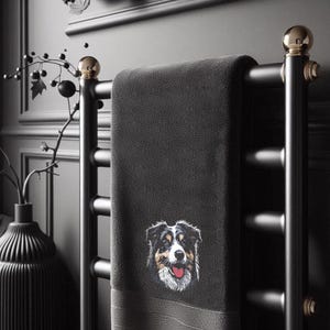 Maschinenstickdatei eines flauschigen Australian Shepherds, hochwertig gestickt auf ein dunkles Handtuch in einem modern eingerichteten Badezimmer mit einer schwarzen Designer-Vase und Trockenblumen im Hintergrund von LunaChild.com