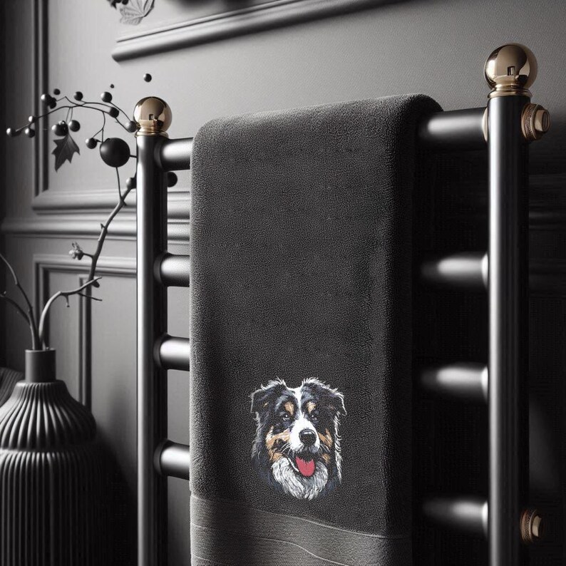 Maschinenstickdatei eines flauschigen Australian Shepherds, hochwertig gestickt auf ein dunkles Handtuch in einem modern eingerichteten Badezimmer mit einer schwarzen Designer-Vase und Trockenblumen im Hintergrund von LunaChild.com