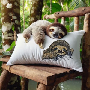 Puede incluir: Una almohada blanca con un perezoso marrón bordado en ella. Un perezoso real está acostado encima de la almohada, mirando a la cámara.