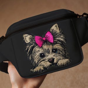 May include: Black fanny pack with a brown and white embroidered Yorkshire Terrier wearing a pink bow.