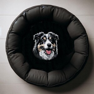 Stickdatei Australian Shepherd Sanzy als exklusives Anwendungsbeispiel für Heimtierbedarf, zentral aufgestickt auf dem schwarzen Plüsch-Liegekissen eines runden, dunkelgrauen Hundebetts in der Draufsicht auf hellem Fliesenboden von LunaChild.com