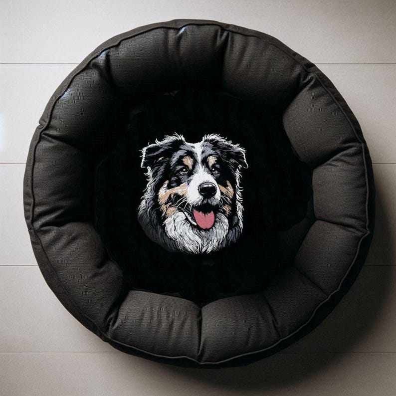 Stickdatei Australian Shepherd Sanzy als exklusives Anwendungsbeispiel für Heimtierbedarf, zentral aufgestickt auf dem schwarzen Plüsch-Liegekissen eines runden, dunkelgrauen Hundebetts in der Draufsicht auf hellem Fliesenboden von LunaChild.com