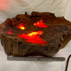 May include: A wooden bowl with a natural edge and a red resin inlay. The resin is lit from within, creating a warm glow. The bowl is approximately 15 inches in diameter.