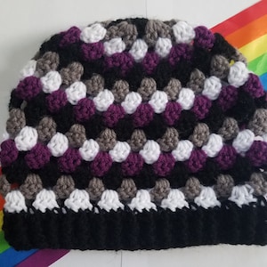 May include: A crocheted beanie hat with a black, white, gray, and purple color pattern. The hat is made with a textured stitch.