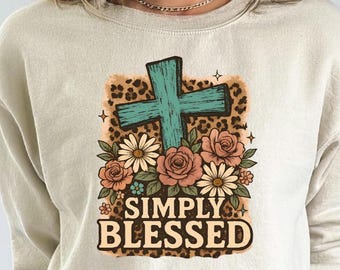 May include: A beige crewneck sweatshirt featuring a central graphic of a teal cross layered over a leopard print background. Below the cross are pink roses and white daisies. The text SIMPLY BLESSED is printed in a bold brown font.