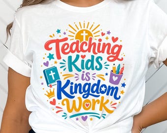 May include: A white t-shirt featuring a colorful graphic with the text "Teaching Kids is Kingdom Work". The design includes a yellow sun with a cross, a blue book with a cross, a purple cup with pencils, a gold crown, and various small hearts and stars.
