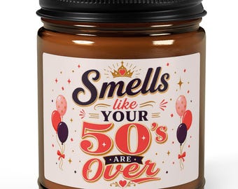 May include: A brown glass candle jar with a black lid featuring a white label that reads Smells like your 50's are over in red and dark blue text, decorated with illustrations of red, pink, and dark purple balloons and a small gold crown.
