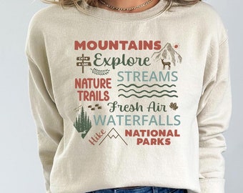May include: A beige sweatshirt with a graphic print of mountains, streams, nature trails, fresh air, waterfalls, and national parks. The text is in a vintage style font.