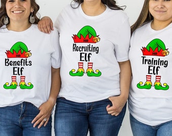 May include: Four white t-shirts featuring a graphic of a green and red elf hat, striped elf legs, and text reading Administrative Elf, Benefits Elf, Recruiting Elf, and Training Elf, each with HR printed on the hat.