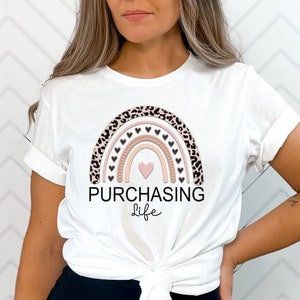 May include: White t-shirt with a pink and brown rainbow design featuring black hearts and a leopard print. The text "PURCHASING life" is printed below the rainbow.