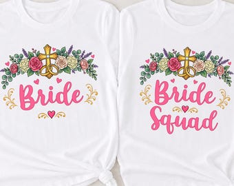 May include: Two white short-sleeved t-shirts featuring a floral graphic with a gold cross and rings. One shirt displays the pink text Bride, while the other displays the pink text Bride Squad. Both shirts have a knotted hem and a crew neckline.