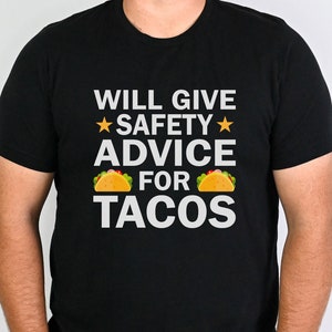 May include: A black t-shirt with the text "WILL GIVE *SAFETY* ADVICE FOR TACOS" in white. Two yellow taco illustrations are on either side of the text.