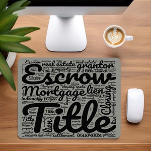 May include: A gray mousepad with a black word cloud featuring real estate terms like "Escrow", "Mortgage", "Title", "Lien", "Closing Costs", "Settlement", "Insurance", and "Grantor".
