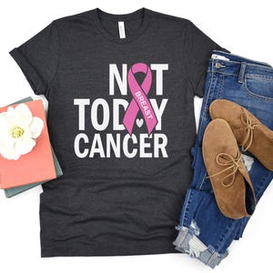 May include: A dark gray t-shirt with the text "Not Today Cancer" and a pink ribbon with the word "Breast" on it.