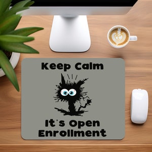 May include: A gray mousepad with the text "Keep Calm It's Open Enrollment" and a black cartoon cat with blue eyes.