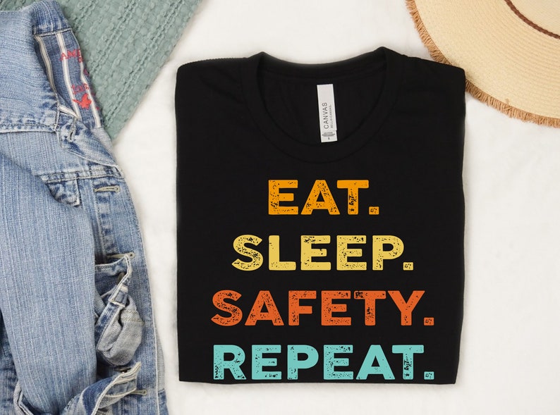 May include: Black t-shirt with a vintage-style graphic that reads "Eat. Sleep. Safety. Repeat."