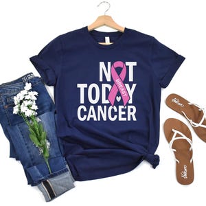 May include: A navy blue t-shirt with the text "NOT TODAY CANCER" and a pink ribbon with the word "BREAST" on it.