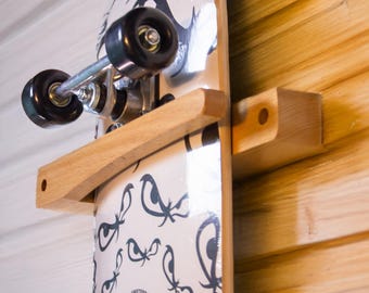 May include: A skateboard mounted on a wooden wall rack. The skateboard has a white surface with a black eye pattern and the text "NO FEAR". The rack is made of light-colored wood and is attached to a wood-paneled wall.