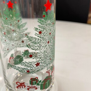May include: A clear glass tumbler with a Christmas tree design. The tree is green with red ornaments and a red star on top. There are also presents at the bottom of the tree.