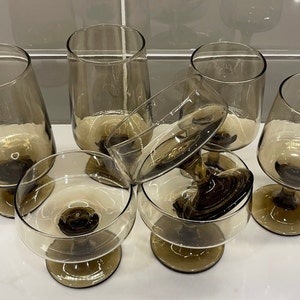 May include: Set of six brown glass stemmed drinking glasses. The glasses are all different shapes and sizes, and some are upside down.