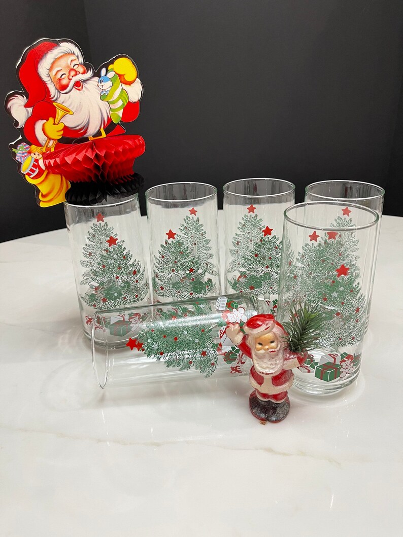 May include: Set of six clear glass tumblers with a Christmas tree design. The glasses feature a green Christmas tree with red stars and presents.