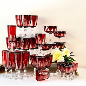 May include: A collection of 24 vintage red wine glasses with a cut glass design. The glasses are arranged in a pyramid shape with a bouquet of white flowers in front.