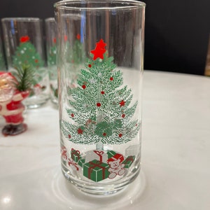 May include: Set of six clear glass tumblers with a Christmas tree design. The tree is green with red ornaments and a red star on top. There are presents and a teddy bear at the base of the tree.