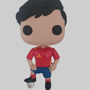 Könnte beinhalten: Eine Funko Pop-Figur eines Fußballspielers in einem roten Trikot mit gelben Akzenten und blauen Shorts. Die Figur hat schwarzes Haar, schwarze Augen und steht auf einem Fußball. Die Figur trägt schwarze Schuhe und rote Socken.