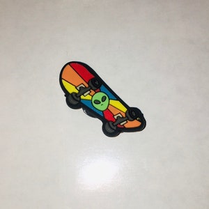 May include: A rainbow-colored skateboard with black wheels and a green alien face graphic.