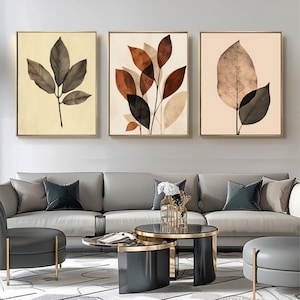 Könnte beinhalten: Drei gerahmte Drucke mit abstrakten Blattmotiven in Braun-, Beige- und Schwarztönen. Die Drucke hängen an einer weißen Wand über einem grauen Sofa.