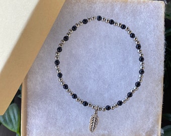 Black and Silver coloured beaded stretch bracelet with an feather charm